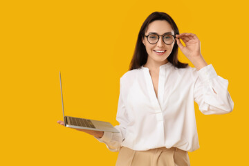 Pretty young woman with modern laptop on yellow background