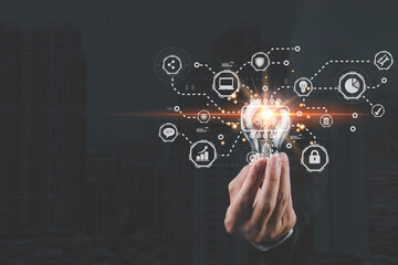 A hand holding a glowing light bulb with digital icons representing ideas, technology, and communication in the background.