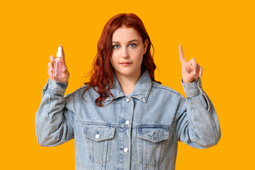 Beautiful young woman with bottle of sanitizer pointing at something on yellow background
