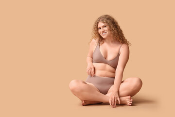 Beautiful young happy body positive woman in trendy underwear sitting on beige background