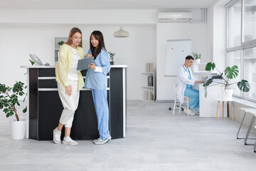 Female Asian medical intern working with patient near reception in clinic