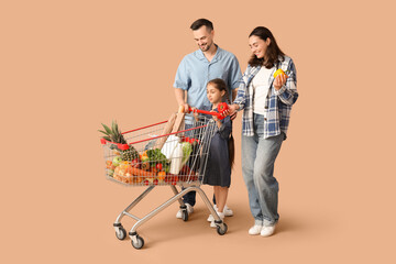 Happy family with full shopping cart and bell peppers on beige background
