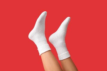 Legs of young woman in white cotton socks on red background