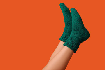 Legs of young woman in green knitted socks on orange background