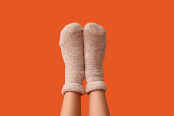 Legs of young woman in warm beige socks on orange background