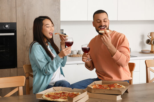 Young couple with wine eating pepperoni pizza in kitchen