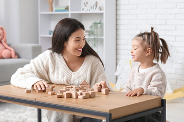 Cute little girl with teacher and cubes learning alphabet at table in room