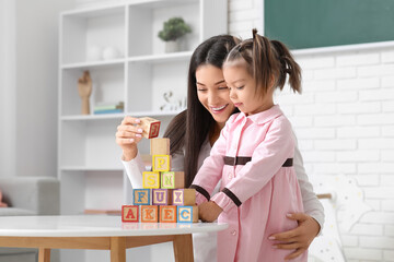 Female teacher with cubes and little girl learning alphabet at home