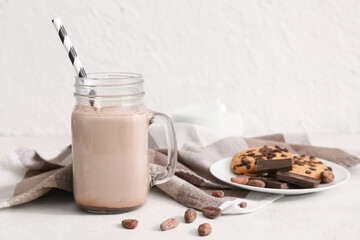 Mason jar of sweet chocolate milk with tasty cookies and cocoa beans on white background