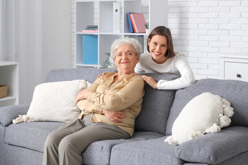 Smiling nurse hugging senior woman on sofa at home