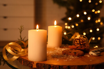 Composition with burning candles, cookies and decorations on table against Christmas tree indoors