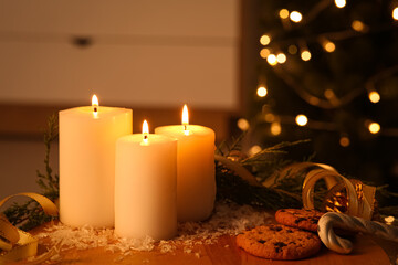 Composition with burning candles, cookies and decorations on table against Christmas tree indoors