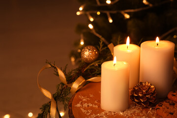 Burning candles and Christmas decorations on table against Christmas tree in evening