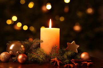Composition with burning candle, fir branches, decorations and spices on table against Christmas tree