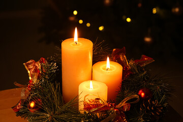 Composition with burning candles and Christmas wreath against decorated fir tree in evening