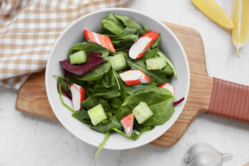 Bowl of salad with crab sticks, spinach and cucumber on white grunge background