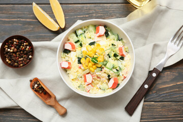 Bowl of salad with crab sticks, corn and cucumber on wooden background