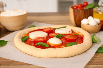 Raw pizza with mozzarella and ingredients on table in kitchen