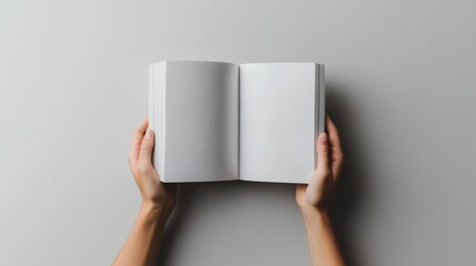 39.A top-view image of hands holding an open magazine with smooth, unmarked pages, against a soft grey background, emphasizing simplicity and focus on the blank space.