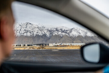 airplane taking off against a backdrop of snow-capped mountains, framed by the interior person driving car window