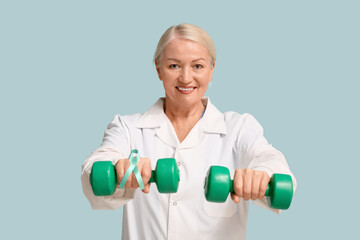 Mature female doctor with teal ribbon and dumbbells on blue background. Cervical Health Awareness...