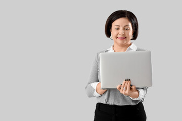Mature businesswoman working with laptop on light background