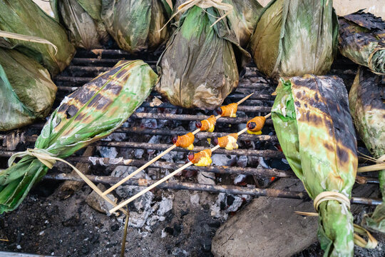 Ecuadorian South American Amazon rainforest indigenous tribe barbecue of banana leaf wrapped meat, seafood and corn with grubs (Chontacuros) entomophagy on wooden skewers on the charcoal grill