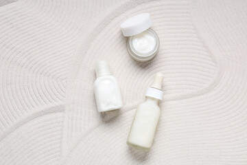 Jar and bottles with cosmetic products on white sand as background