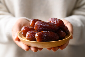 Date palm fruit (MedJool) on wooden plate holding by hand