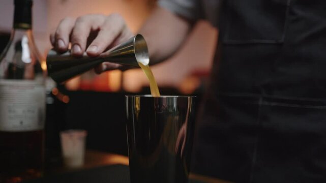 Craft cocktail pouring from jigger to shaker in cozy home bar. Perfect for bartender tutorials or cocktail recipe videos.