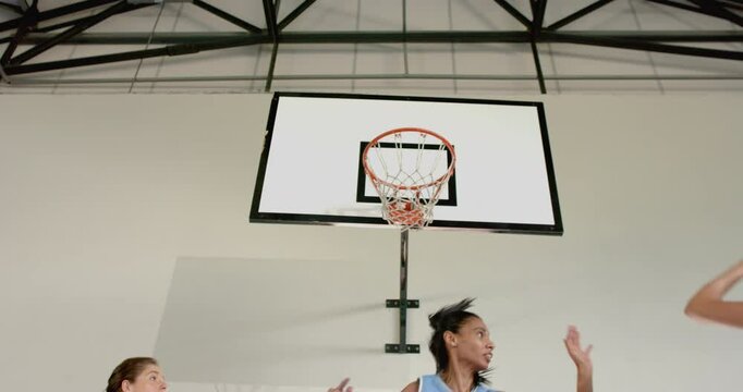 Playing basketball, women reaching for ball near hoop in indoor court