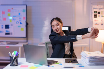 Young asian businesswoman wearing a suit is sitting at her desk in a modern office at night,...