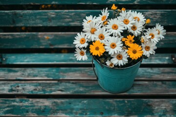 Fototapeta premium Daisies and yellow flowers in a teal bucket on wood