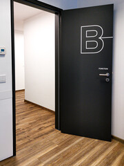 Modern black door with a bold letter B and signage in a contemporary interior hallway