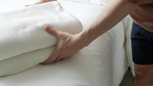 Asian man housekeeping cleaning bed make up room arranging placing towel on white linen bed in bedroom hotel resort,set up white tower on the bed in bedroom resort hotel ready for guest to check in