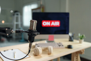 Professional condenser microphone is broadcasting live on air in a home studio, with a computer displaying the on air sign in the background, creating a professional and engaging broadcasting setup