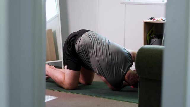 Young Caucasian man doing the back stretch yoga exercise in the house during daytime