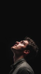Side studio portrait of a man looking up while holding a mobile phone, isolated against a black background, with ample empty space above for text or graphic elements, portrait, technology, communicati