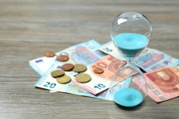 Modern hourglass and Euro banknotes and euro cents on wooden background. Hourglass time concept for business deadline, urgency and outcome of time