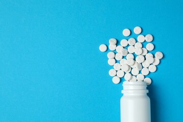 White pills pouring out of medicine bottle on colorful background