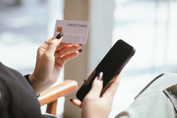 Close-up of young Asian woman using smartphone and credit card for mobile banking or online shopping. She represents modern e-commerce, digital transactions and financial technology.