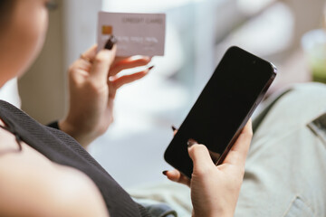 Close-up of young Asian woman using smartphone and credit card for mobile banking or online shopping. She represents modern e-commerce, digital transactions and financial technology.