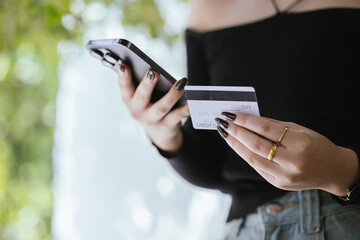 Close-up of young Asian woman using smartphone and credit card for mobile banking or online shopping. She represents modern e-commerce, digital transactions and financial technology.