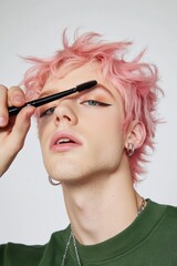 Obraz premium Young man with pastel pink hair applying mascara in a beauty product advertisement with a soft glam makeup look