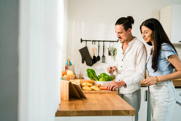 A couple prepares fresh ingredients in a bright kitchen, smiling and enjoying their time together while using a tablet for cooking inspiration. Couple spend quality time in a relationship