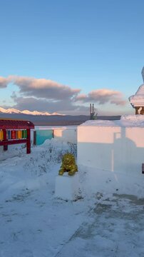 Vertical video of  Buddhist prayer complex with white stupa or suburgan and prayer drums against backdrop of snow-capped mountains of Eastern Sayan at winter sunset. Buryatia. Tunka valley