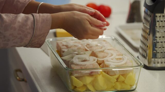 Woman cooking fish cod baked in oven with vegetables at home. Potatoes and cod fish fillet in oven baking dish. Healthy diet healthy food.