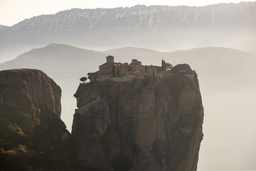 Travel to Meteora. The Monastery of Holy Trinity photographed in amazing sunset light with mountains in foreground. Travel to Orthodox iconic place of Meteora in Greece.
