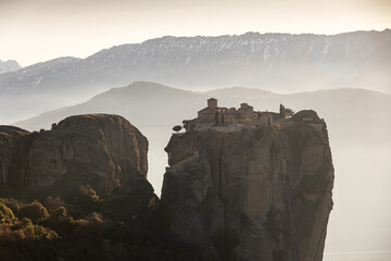 Travel to Meteora. The Monastery of Holy Trinity photographed in amazing sunset light with mountains in foreground. Travel to Orthodox iconic place of Meteora in Greece.