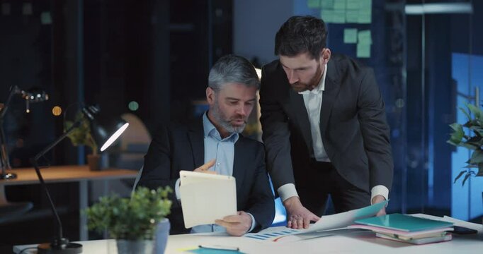 Cooperative caucasian men discussing company strategy start-up solution business ideas in night office interior. Brainstorming. Overworking. Meeting.